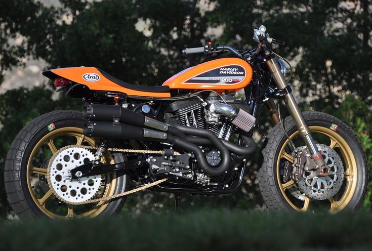 an orange and black motorcycle parked in front of some trees with gold rims on it