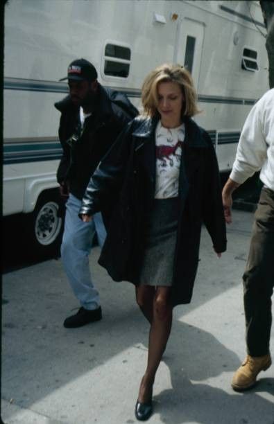 a woman walking down the street in front of a white bus and two men standing next to her