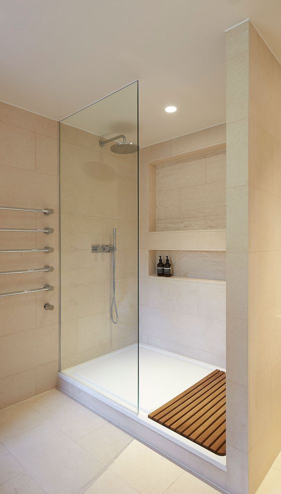 a bathroom with a walk in shower next to a wooden bench and white tiled walls