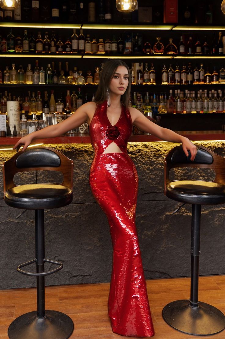 a woman in a red dress standing next to two bar stools with bottles behind her