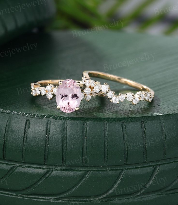 two rings with pink and white stones on them sitting on top of a green surface