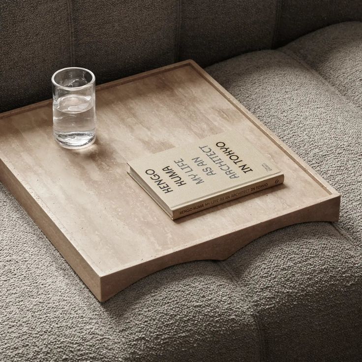 a wooden tray with a book on top of it next to a glass of water