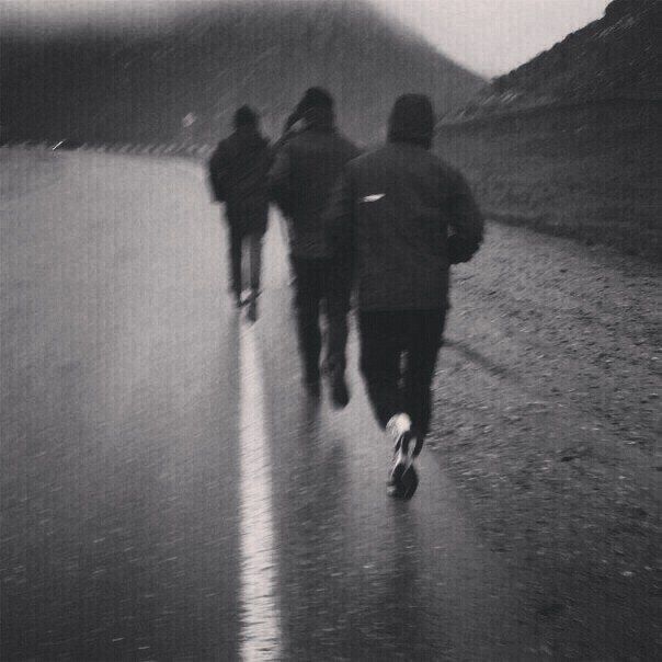 black and white photograph of three people running down the road on a rainy day in the rain