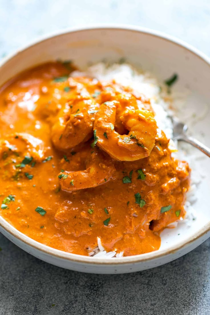 a white bowl filled with shrimp and rice on top of a blue tablecloth next to a spoon