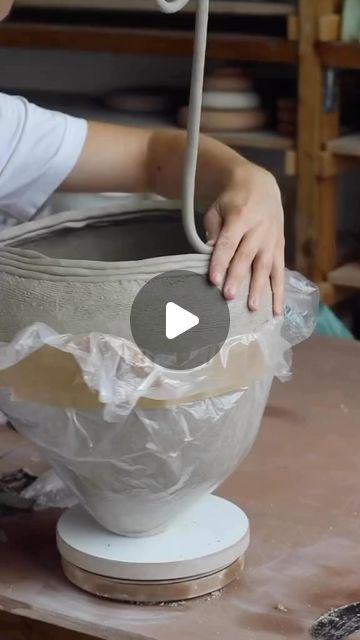 a person is making a bowl out of clay and plastic wrap around the base with their hands