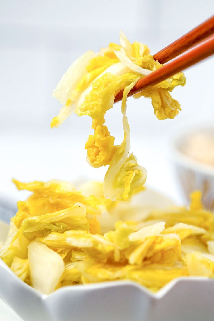 chopsticks picking up some food from a white bowl with yellow flowers in it