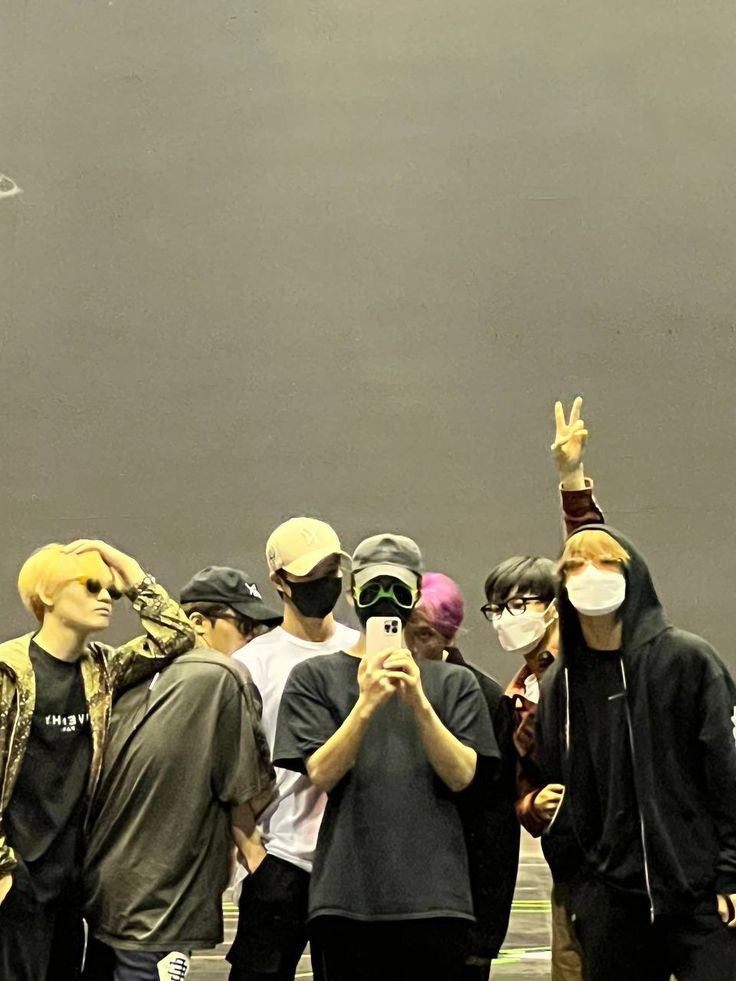 a group of young men standing next to each other wearing face masks and covering their eyes