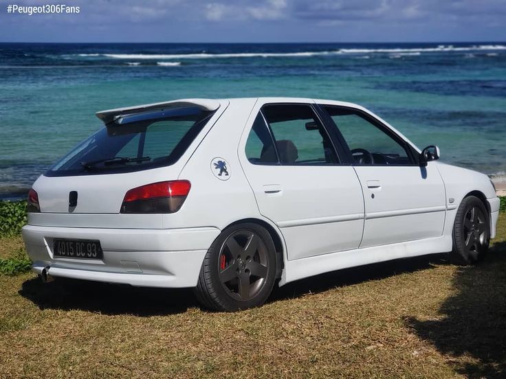 a white car parked on top of a grass covered field next to the ocean