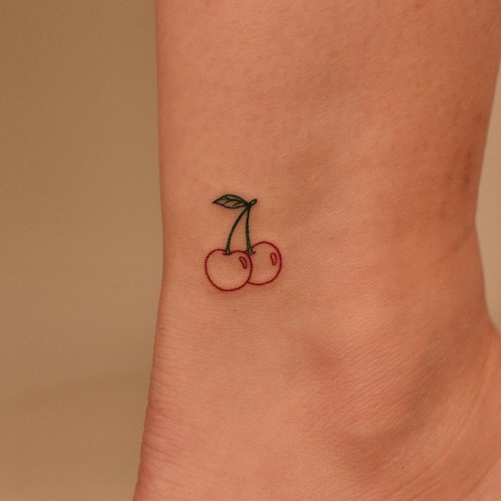 a small cherry tattoo on the side of a woman's ankle, with two cherries attached to it