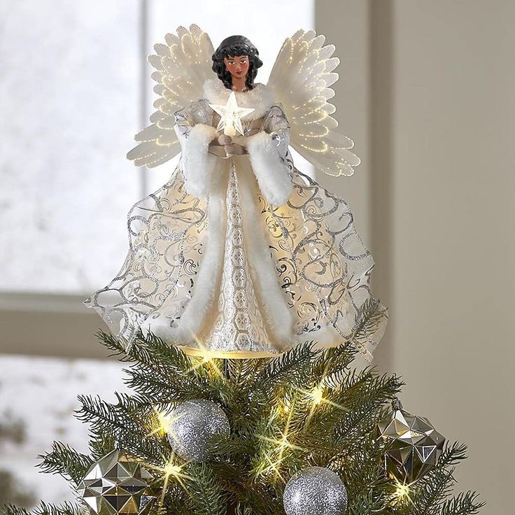 an angel figurine sitting on top of a christmas tree decorated with silver baubies