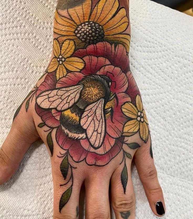 a woman's hand with a bee and flower tattoo on the middle of it