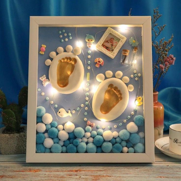 a baby's hand and foot casts are displayed in a shadow box surrounded by blue balls