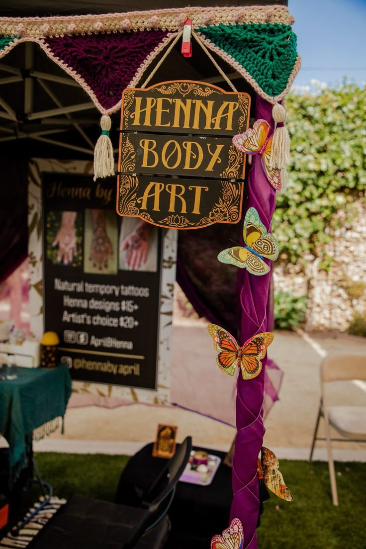 a sign that says henna body art hanging from the side of a tent with butterflies on it