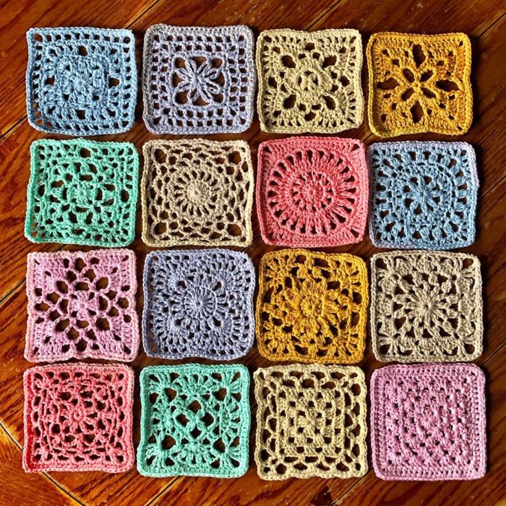 crocheted squares are arranged in rows on the wooden floor, each with different colors