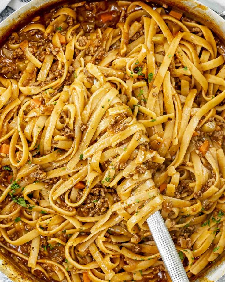 a skillet full of pasta and meat with a spatula in the bottom left corner