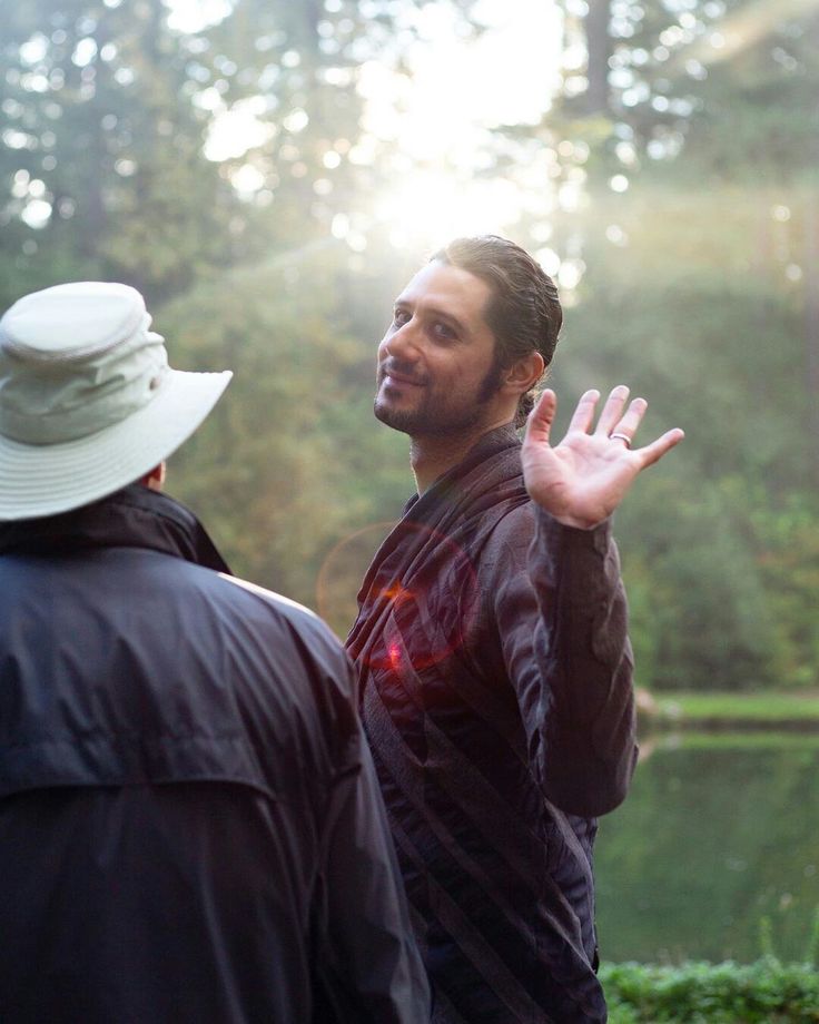 two men standing next to each other in front of trees and sun shining on them