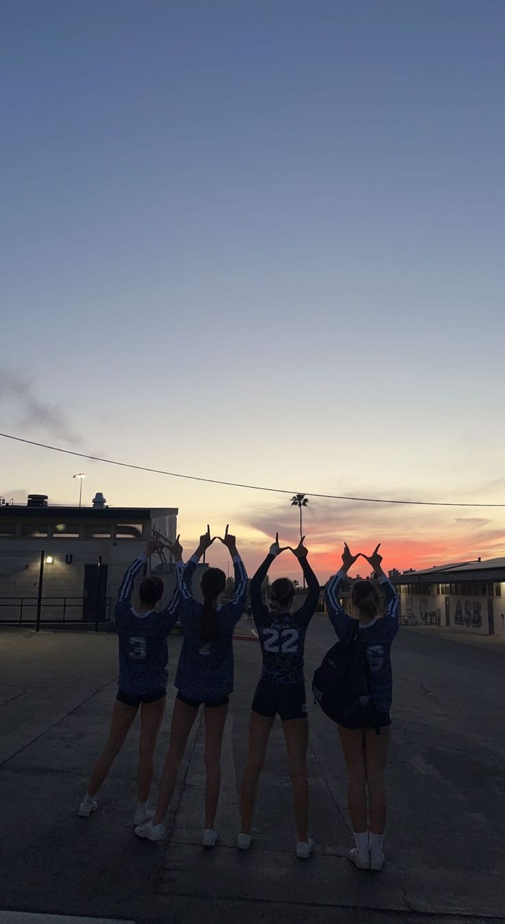 three cheerleaders are holding their hands up in the air while standing on an empty parking lot