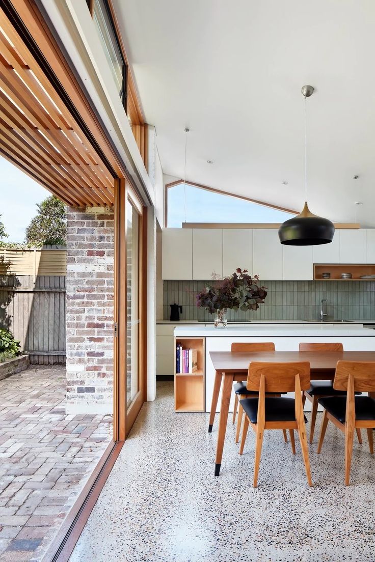 an open kitchen and dining room area with brick walls, flooring and wooden furniture