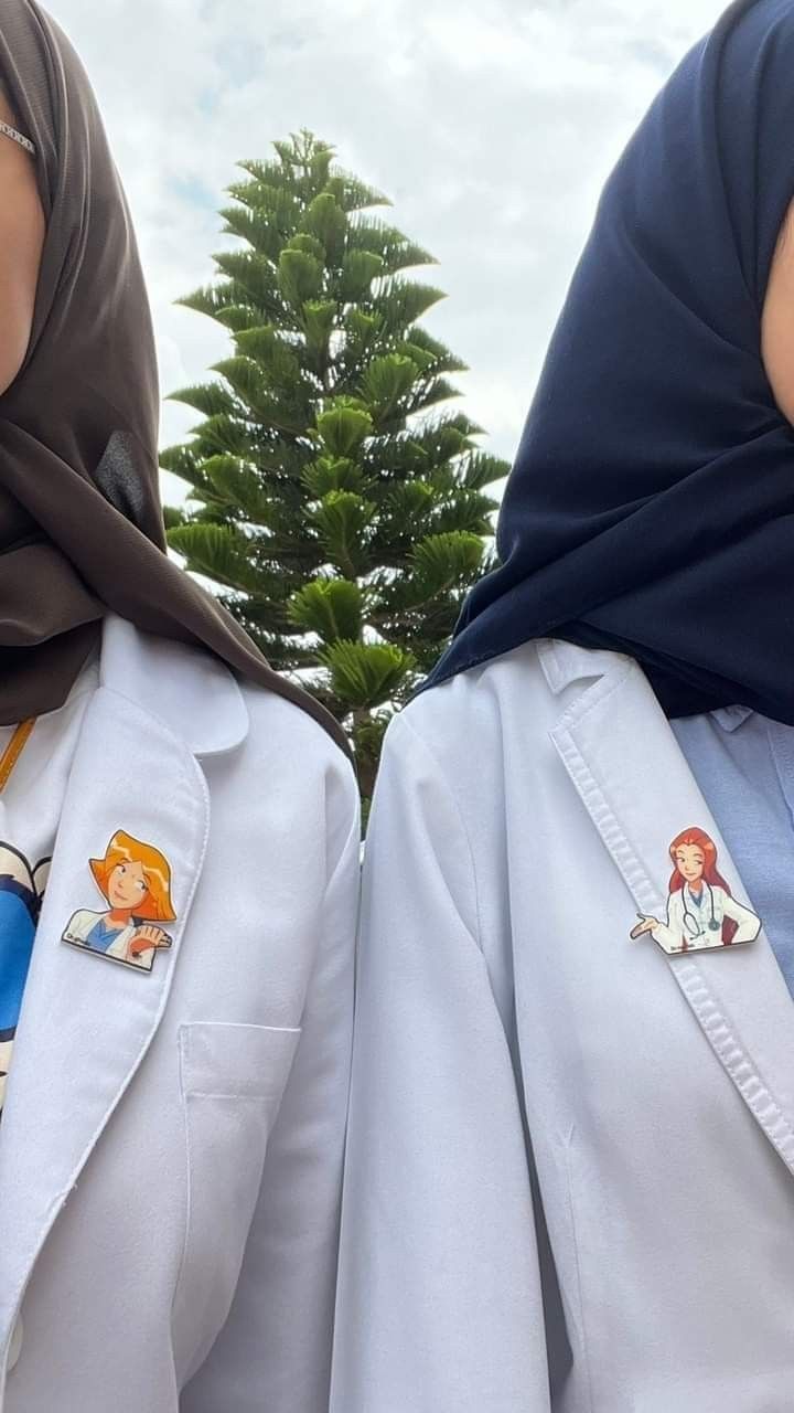 two women wearing white coats with cartoon pins on their lapels and headscarves