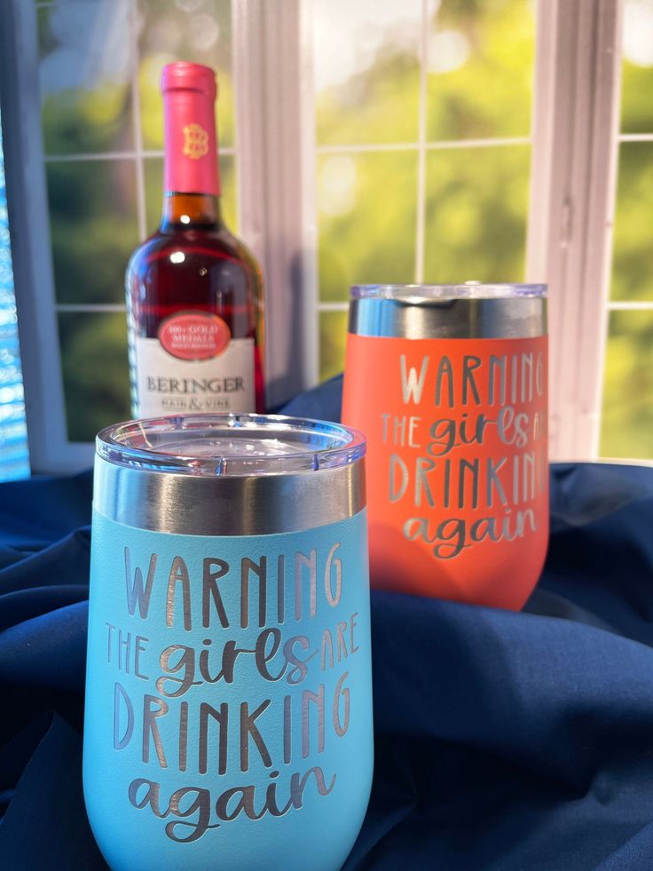 two wine glasses sitting next to each other on a blue table cloth with a bottle in the background