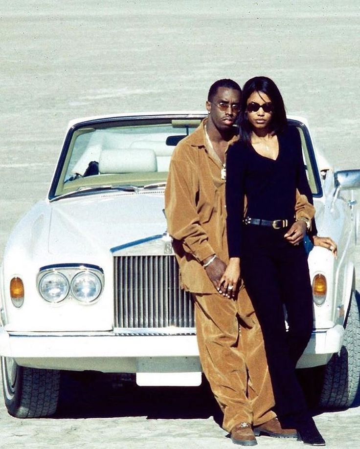 a man and woman standing next to a white car in the sand with their arms around each other