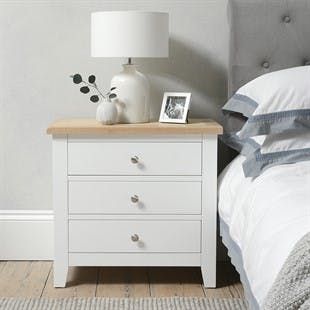 a white nightstand with two drawers and a lamp on top of it next to a bed