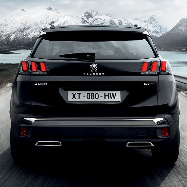 the rear end of a black car driving on a road with mountains in the background