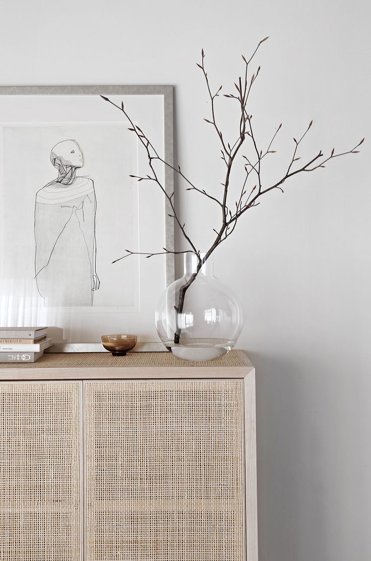 a vase with branches in it sitting on top of a dresser next to a framed drawing