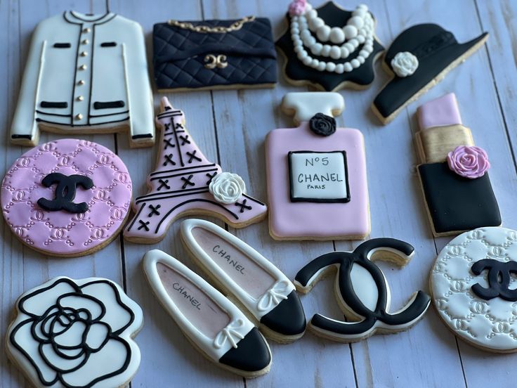 many decorated cookies are arranged on a white table with pink and black accents, such as chanel