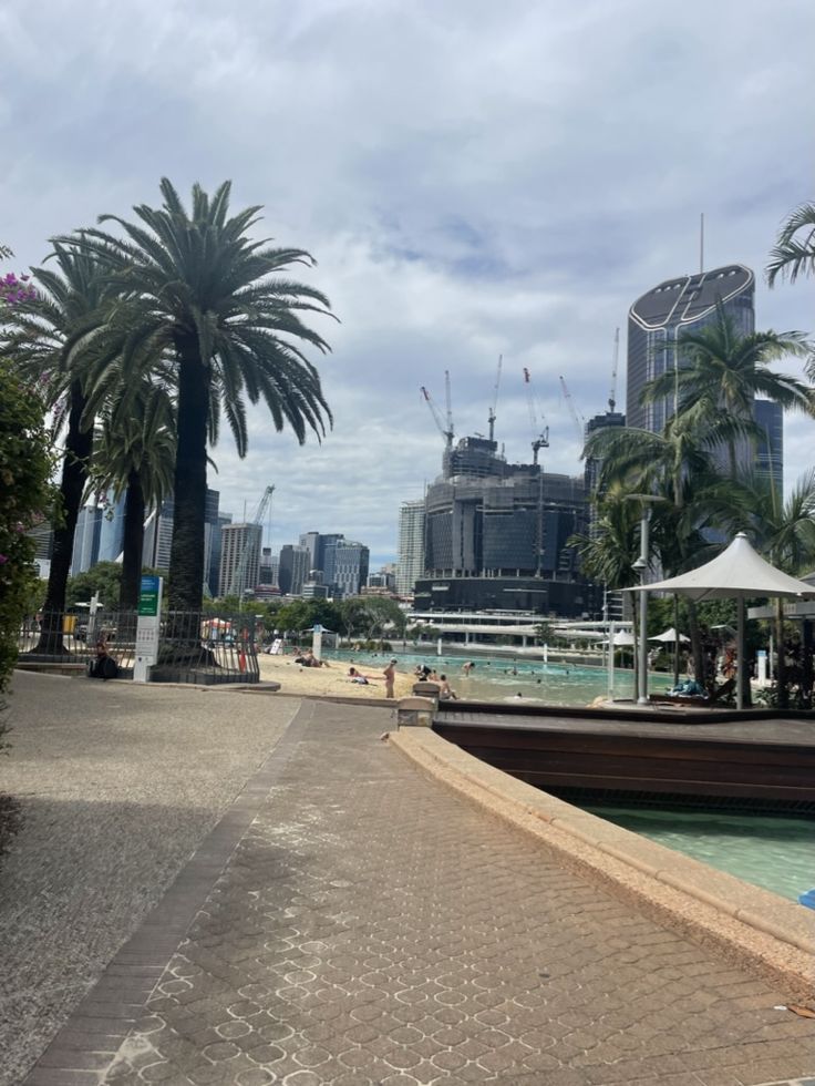 palm trees are in the foreground, and people walk on the other side of the water