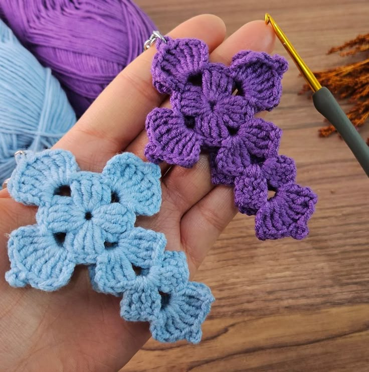 two crocheted flowers are being held by someone's hand with yarn in the background