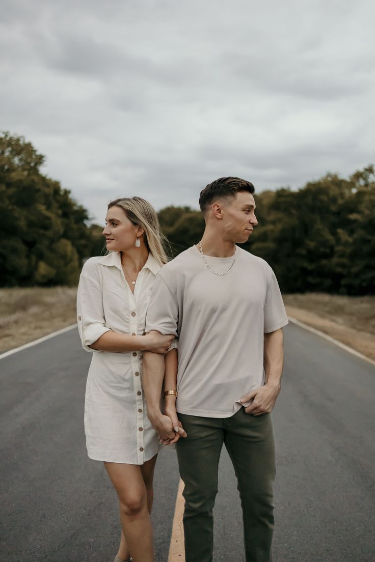 a man and woman walking down the middle of an empty road with trees in the background