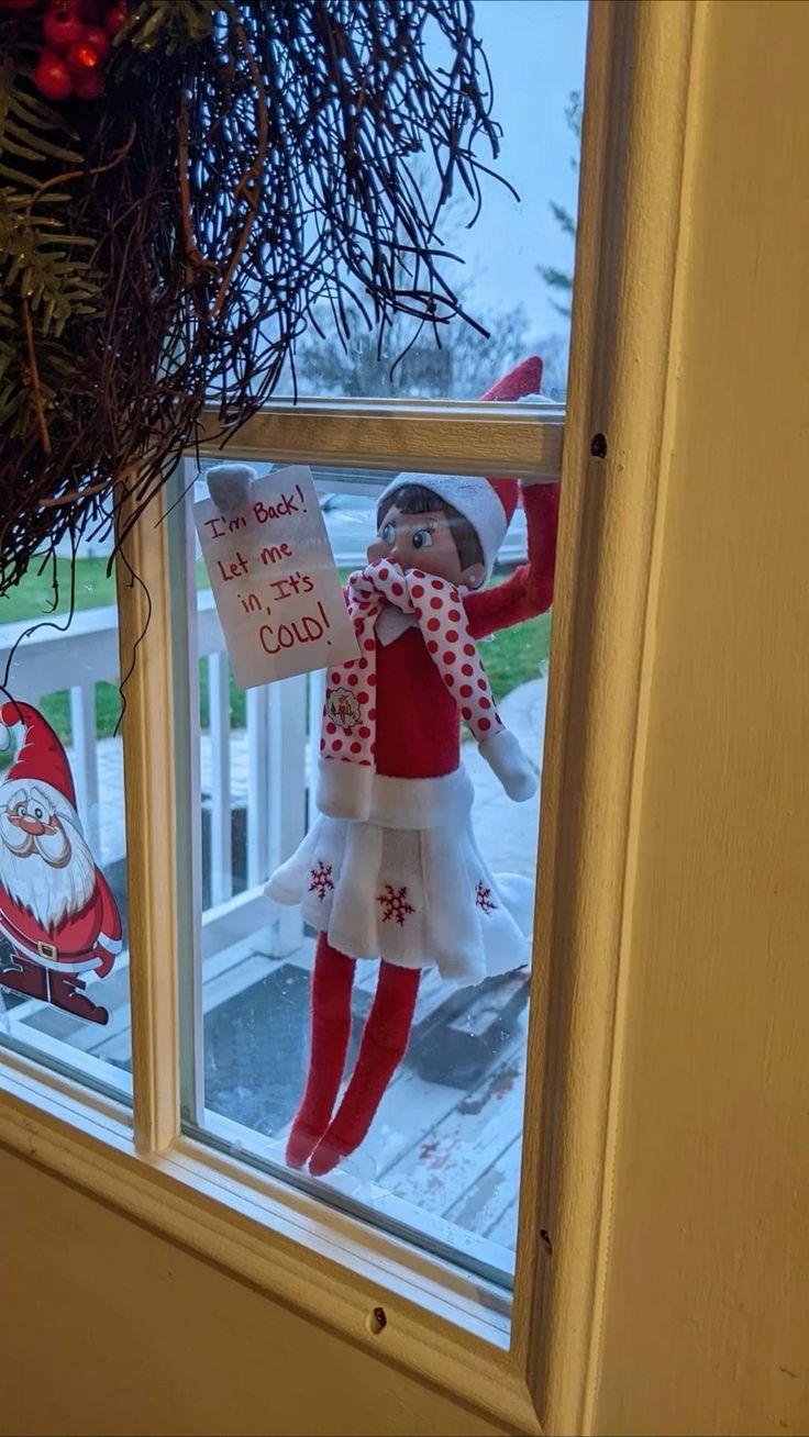 an elf is hanging on the window sill with a sign that says it's christmas