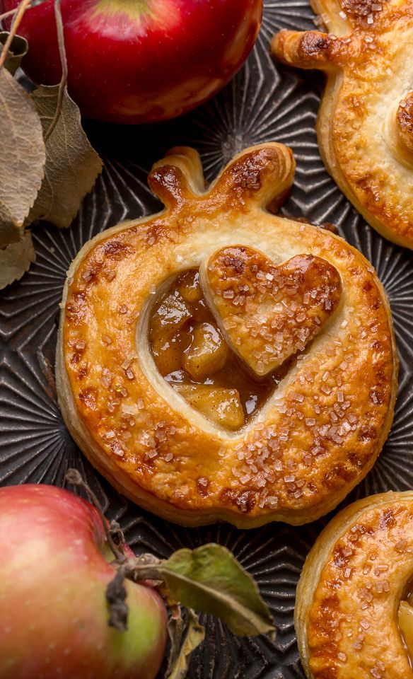 apple pies on a plate with apples and leaves around them in the shape of a heart