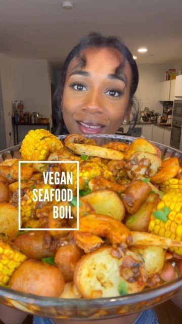 a woman is holding a large bowl full of vegetables and potatoes with the words vegan seafood boil in front of her