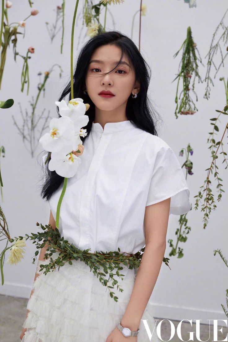 a woman with long black hair wearing a white dress and holding a flower in her hand