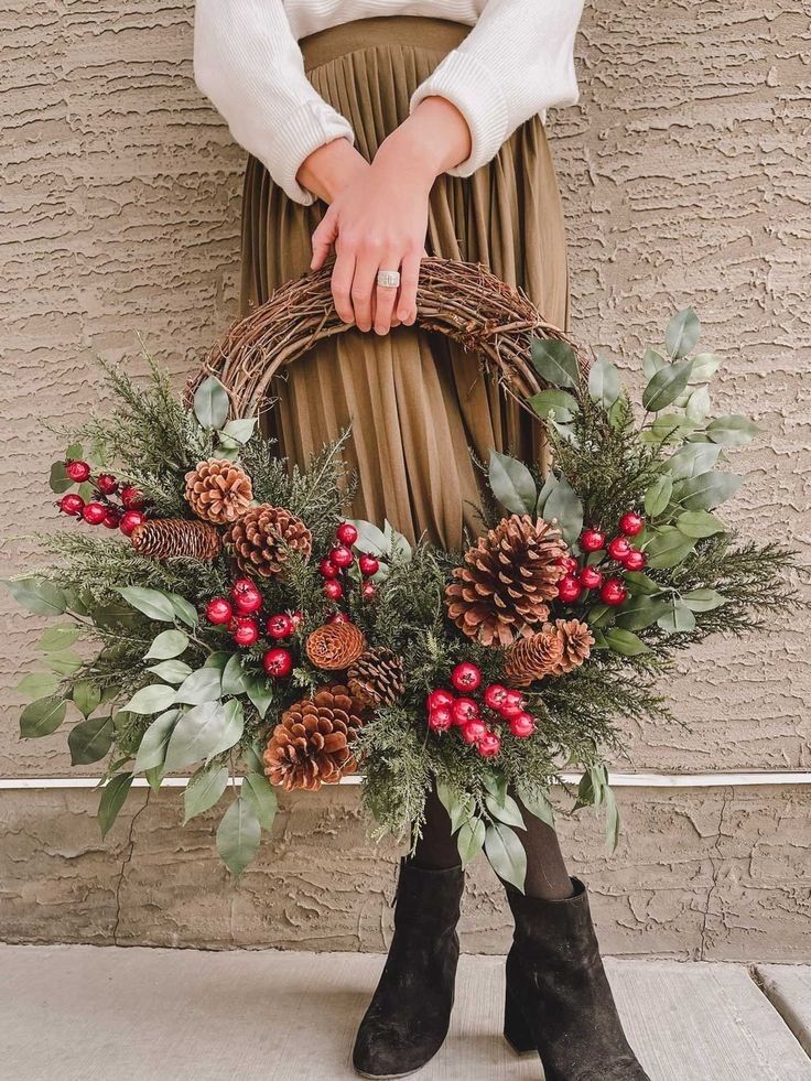 a woman holding a wreath with pine cones and berries