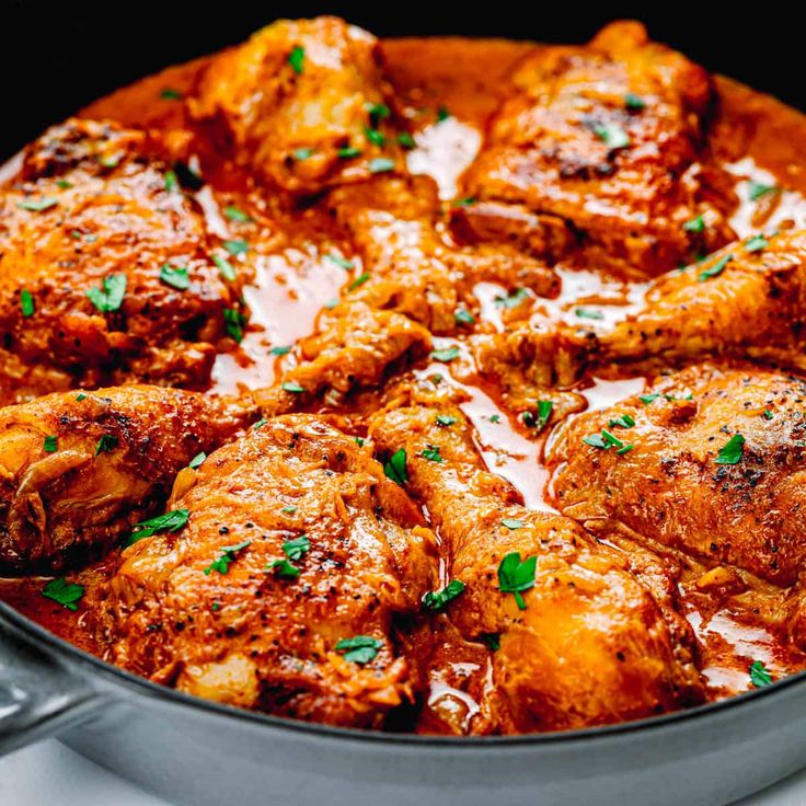 a pan filled with meat covered in sauce and garnished with fresh parsley