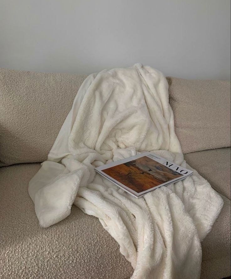 an open laptop computer sitting on top of a couch covered in a white blanket next to a pillow