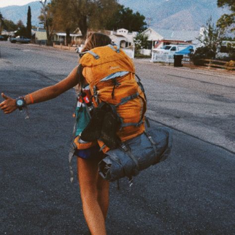 a woman walking down the street with a backpack on her back and one hand in the air