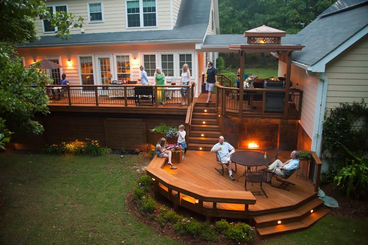 people are sitting on the back deck of a house at night with their lights on