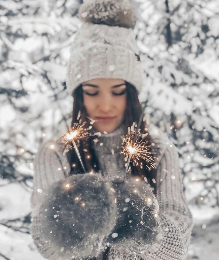 a woman holding sparklers in her hands while wearing winter clothes and a white hat