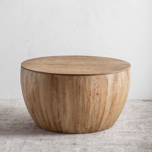 a round wooden table sitting on top of a carpeted floor next to a white wall