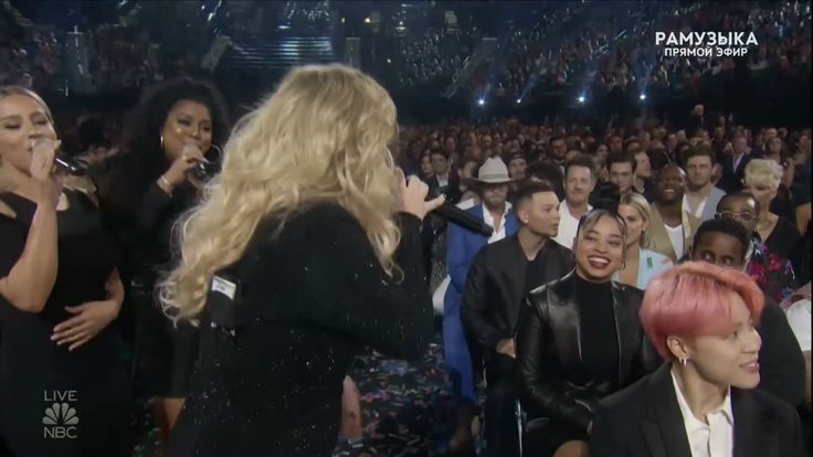 two women with pink hair are standing in front of an audience and one woman is singing into a microphone