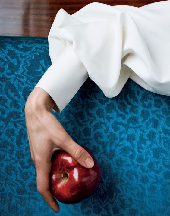 a person holding an apple on top of a blue carpeted floor in front of a wooden table