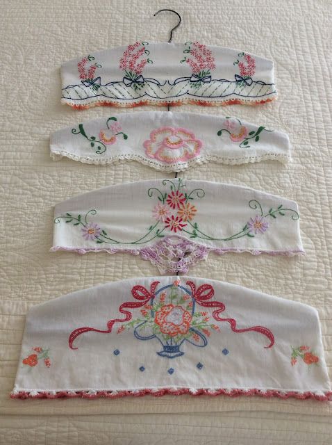 four pieces of embroidered clothing hang on a bed with white linens and pink flowers