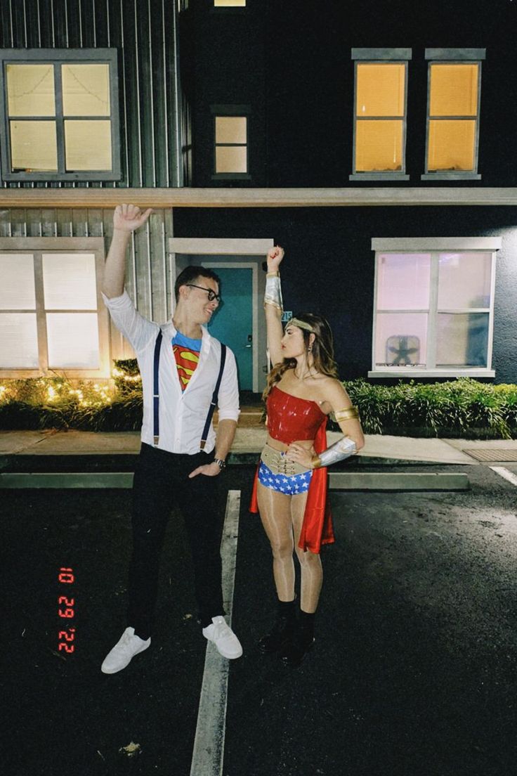 a man and woman dressed up as superman and wondergirl standing in front of a house