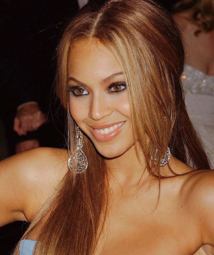 a close up of a woman with long hair wearing earrings and smiling at the camera