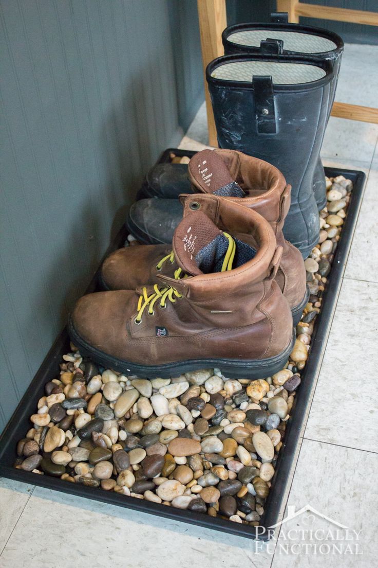 several pairs of boots sitting on top of rocks in front of a door with a trash can next to them