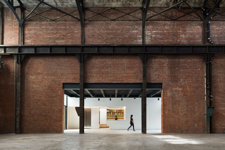 a person walking in an open space with exposed ceilings and brick walls on either side of the room